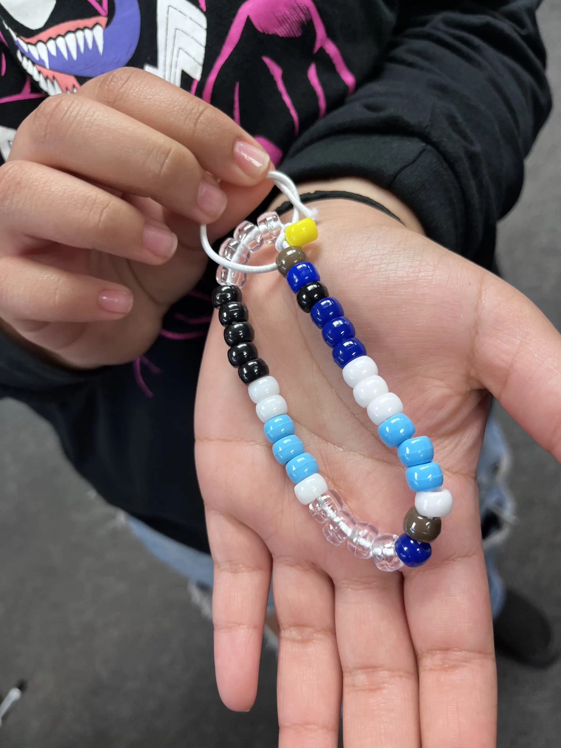 Person holding a keychain made of colorful beads arranged on a plastic loop, reminiscent of assembly programs piecing together intricate designs.